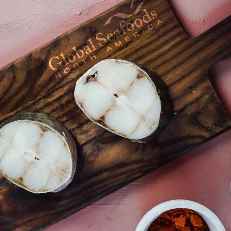 Two sablefish steaks on a wooden board.