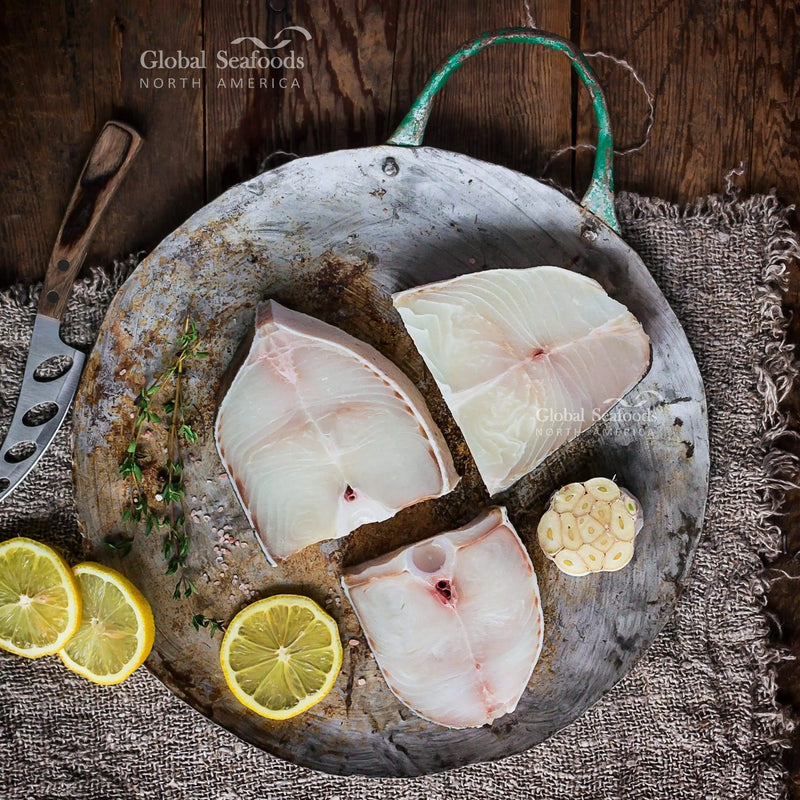 Three raw halibut steaks on a metal tray with lemon and garlic.