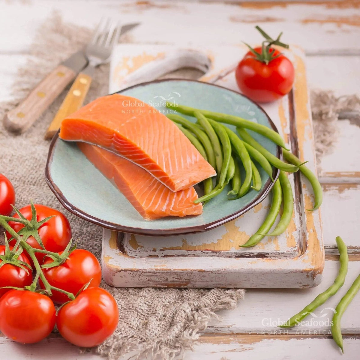 Two raw skin-on sockeye salmon portions on a pale blue plate with green beans and tomatoes nearby.