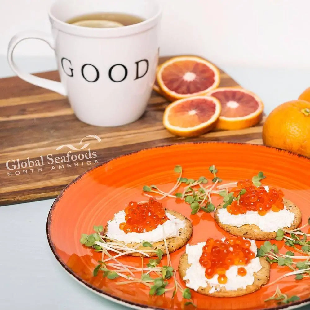 Chum salmon caviar and cream cheese crackers on an orange plate beside a mug and sliced citrus