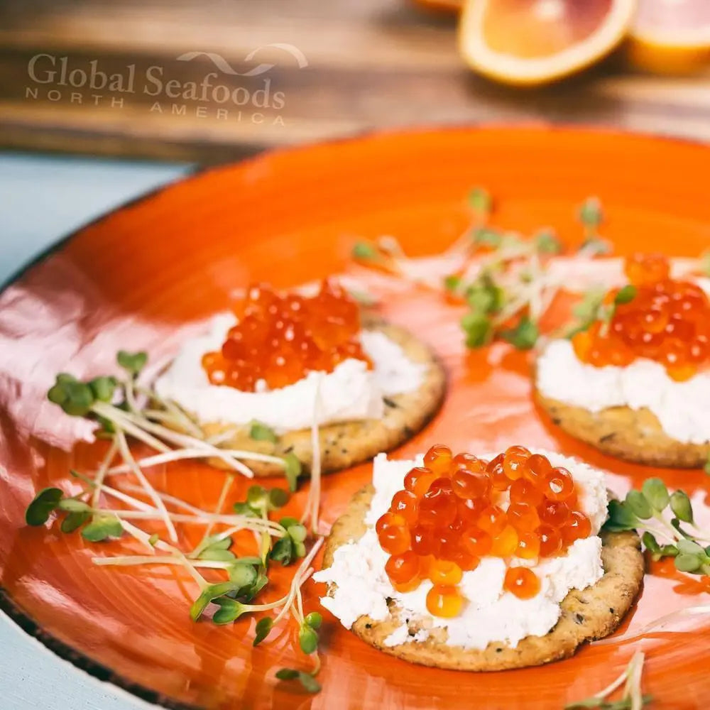 Three crackers topped with cream cheese and chum salmon roe on an orange plate with microgreens