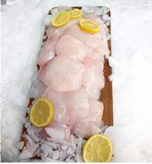 Raw halibut cheeks on a tray over ice with lemon slices.