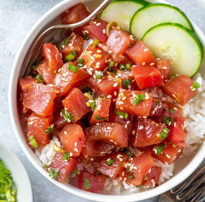 Ahi poke cubes served over rice in a bowl, with sliced cucumber on the side for a fresh and vibrant Hawaiian-style dish